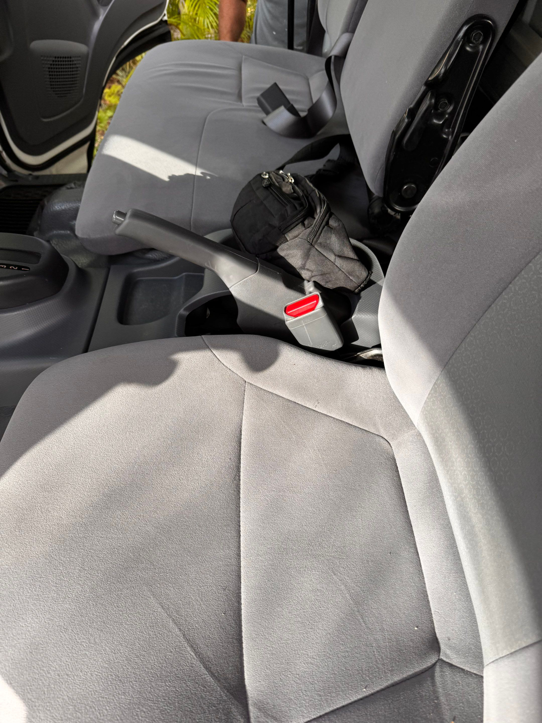 Isuzu NQR interior showing front seats and center console with handbrake, seat belt buckles, and a small black pouch on the passenger seat.