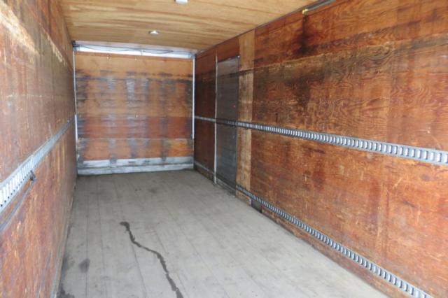 Interior of a box truck cargo area with wood walls and metal E-track rails, empty and well-lit from rear doors.