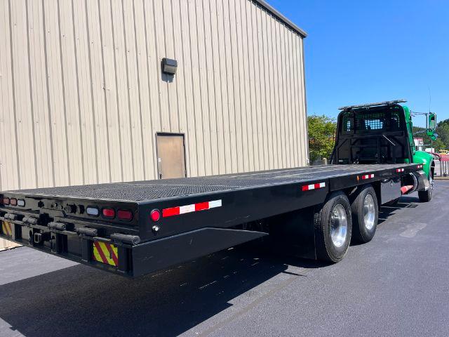 2015 Peterbilt 348 rollback truck with a long flatbed trailer, green cab, dual rear axles, metal diamond plate surface, taillights, and reflective striping.