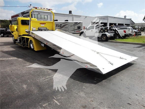 2022 Peterbilt 337 tow truck with a lowered aluminum flatbed in a dealership lot.
