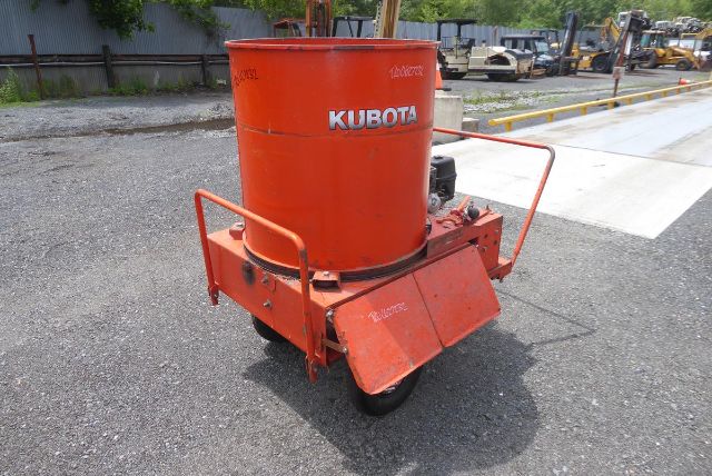 Kubota orange fertilizer mixer on a wheeled frame with a tall cylindrical tank and metal chute in a gravel lot.