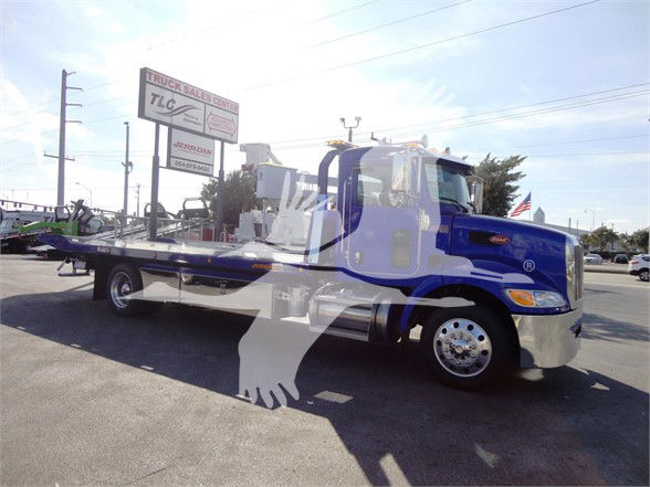 Peterbilt 337 tow truck in blue and chrome, long wheelbase flatbed with equipment in background.
