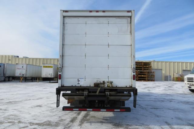 Rear view of a white box truck with a lift gate, showing back doors and bumper; snow on ground; industrial yard with trailers.