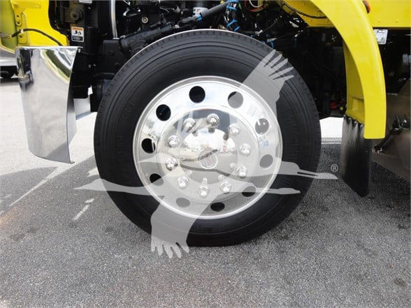 Wheel of a yellow 2022 Peterbilt 337 truck showing chrome hub, lug nuts, and black tire.