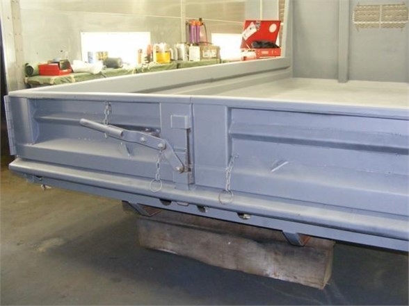 Dump body with rear tailgate and latch hooks, blue metallic paint, forklift pallet beneath, shop background.
