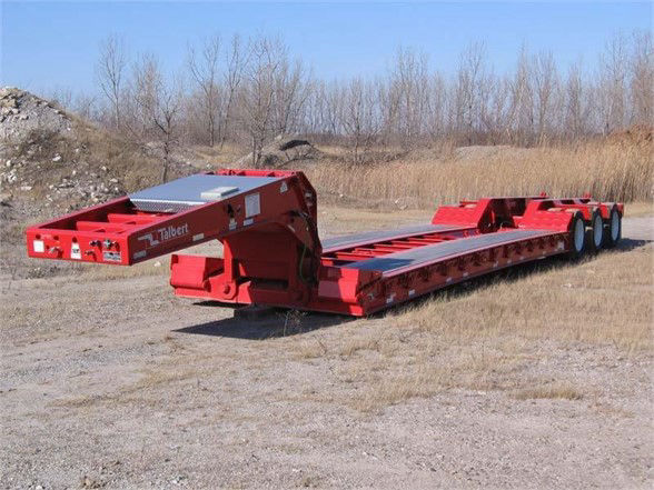 Talbert 55SA flat level deck lowboy trailer with red frame and multiple axles parked on gravel.