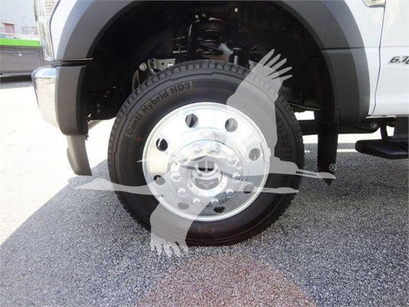 Front wheel and tire of a 2022 Ford F550 dump truck showing chrome hubcap and suspension components visible in wheel well.