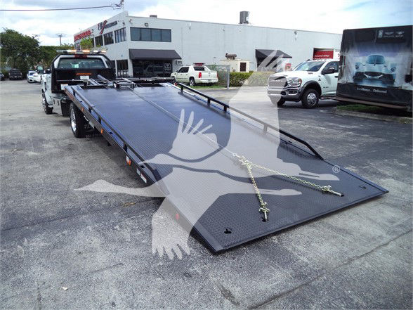 Truck bed with a hydraulic tilt trailer on a dealership lot, chain tie-downs visible, Silverado 6500HD in foreground
