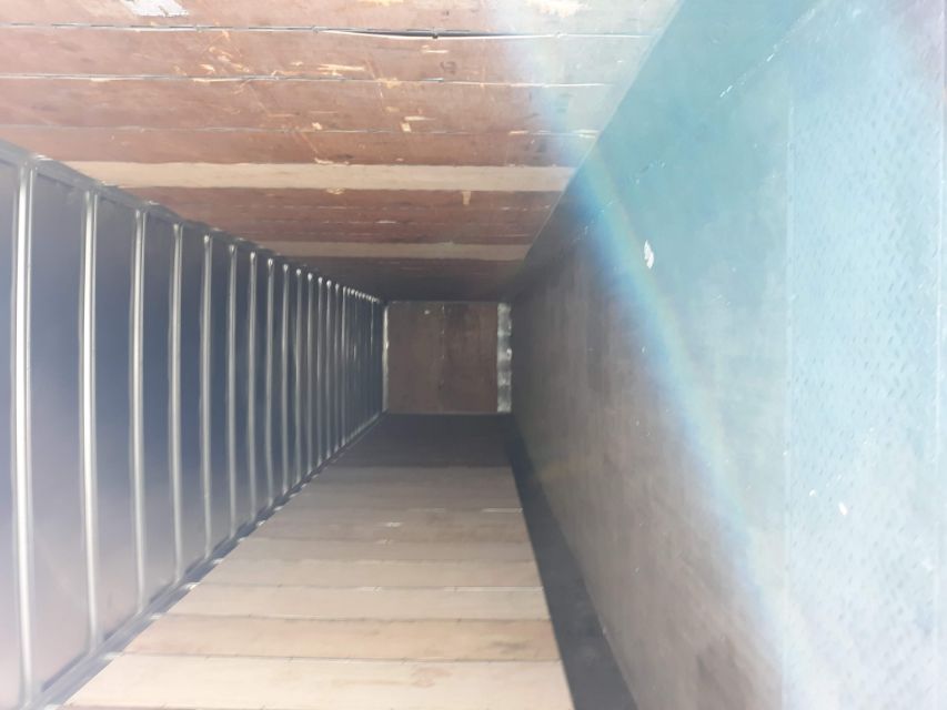 Interior of a cargo trailer with wooden walls and steel ceiling ribs, long narrow framing, empty floor.