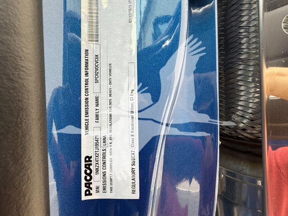Kenworth truck component label displaying vehicle emission information and VIN; PacCAR branding visible on a blue surface.