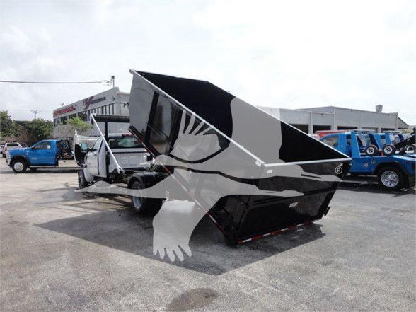 Front view of a 2023 Chevrolet Silverado 5500HD dump truck with its bed raised, showing a white cab and a black dumping bed. Other blue trucks are in the background.