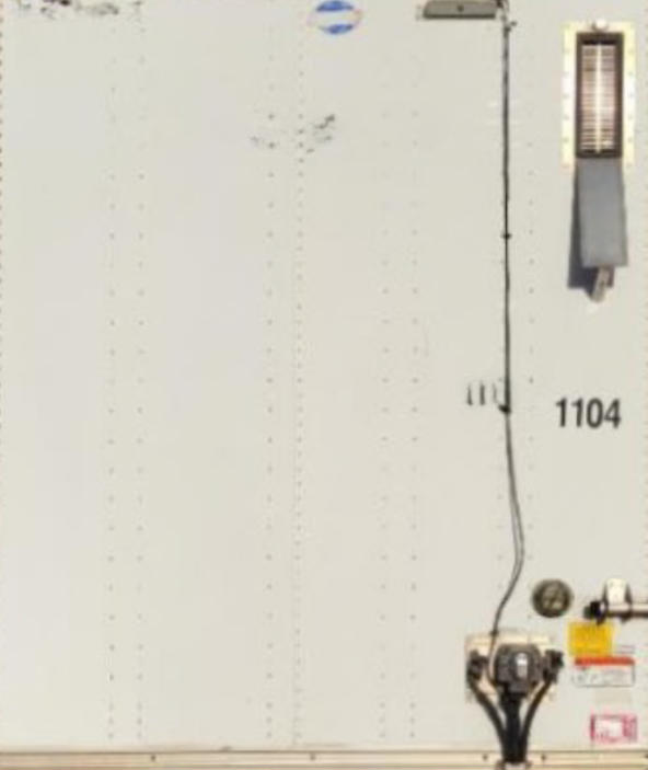 Utility trailer side panel with stock number 1104 and VIN plate area visible, including a latching mechanism and vertical riveted panel lines.