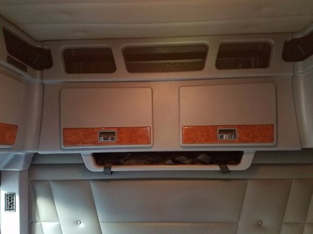 Cab overhead storage compartments with two grey doors and wood-grain panels. Small latching handles on each door; a mesh vent above between the doors.