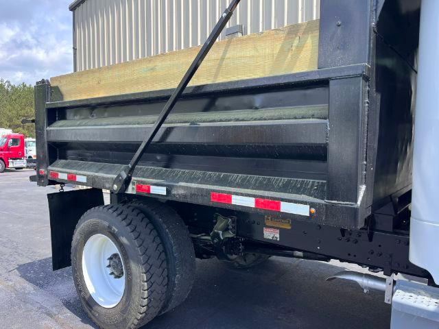 Freightliner M2 106 dump truck bed showing side of cargo box and rear wheel, with black steel dump body and white wheel, reflective tape.