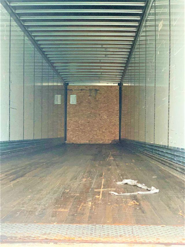 Trailer interior showing empty cargo area with wooden floor, metal sidewalls, and a plywood bulkhead at far end.