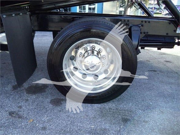 Wheel of Freightliner M2 106 Plus chassis showing chrome hub and tire on a black frame. Overlay watermark of a handshake-style logo.