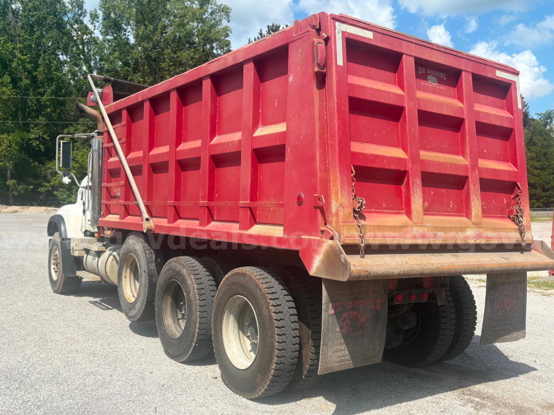 Dump truck bed showing red refuse hopper with rear gate, white cab, and dual rear axles.