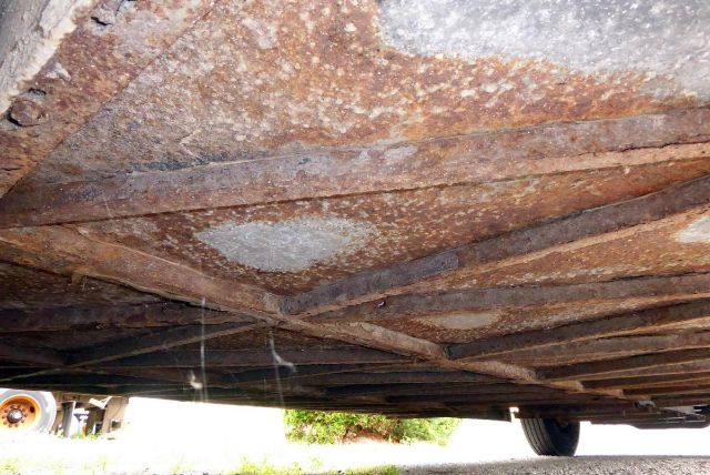 Underbody view of a rusty chassis on a 2005 Bluebird All American bus showing crossmembers and frame rails.
