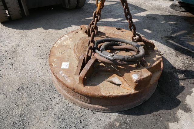 RK Magnetics 57 FDAL lifting ring attached to a rusted circular magnet with chains and hoses in a gravel lot.
