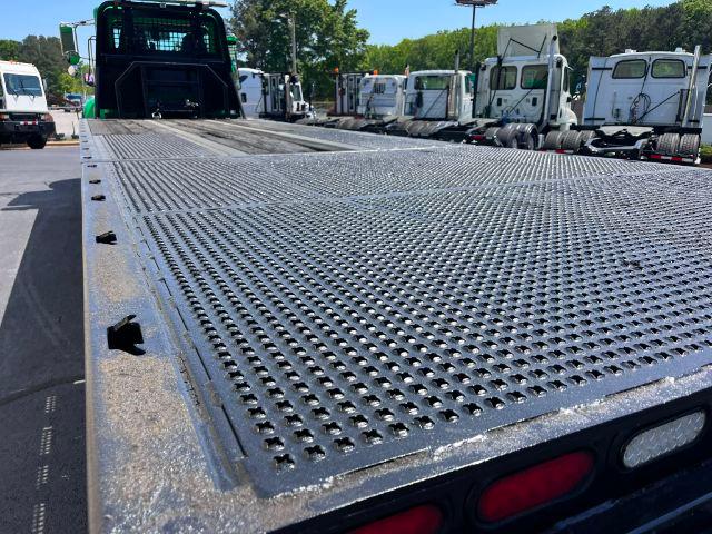 Flatbed with perforated metal surface on a Peterbilt truck. In the background are other trucks and a green cab. Visible text: '2015 Peterbilt 348' in listing context.