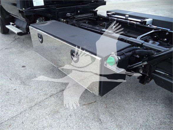 Toolbox mounted under a truck bed with a green cap on a hydraulic reservoir visible; metal toolbox shows latches and a keyhole.