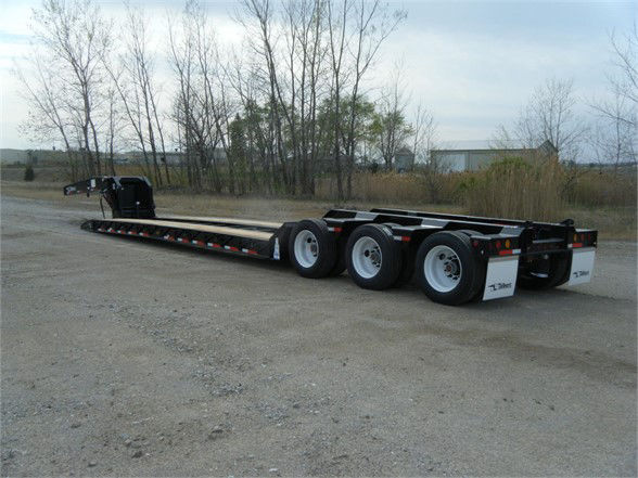 Lowboy trailer with three axles, black frame, white wheels, and a gooseneck neck; no visible text readable on the trailer from this angle.