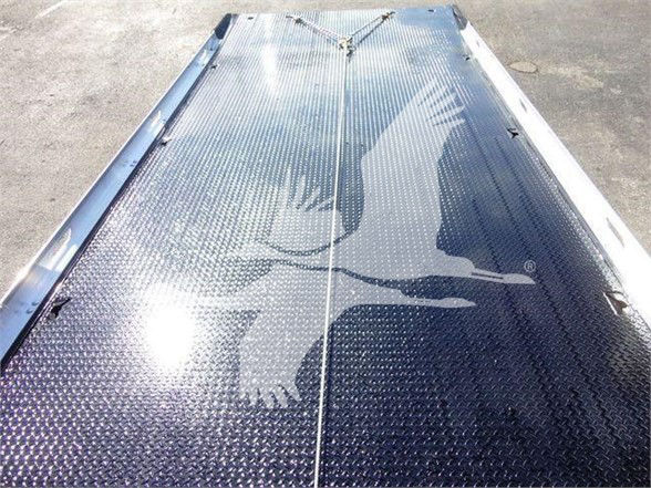 Metal diamond-plate truck bed surface with reflection of sky and surrounding area.