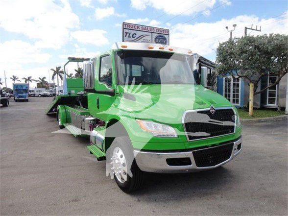 Truck in green and black International MV model showing front view with tow bed equipment in a dealership lot.