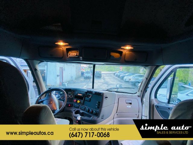 Cab interior of a 2012 Freightliner Cascadia showing dashboard, steering wheel, overhead lights, and windshield.