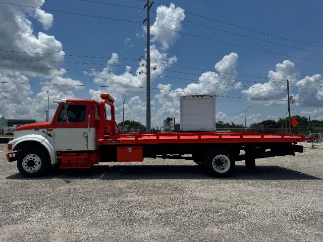 1999 International 4700 DT 466E tow truck with long red flatbed and white cab, side view shows hydraulic equipment and tandem rear axle.