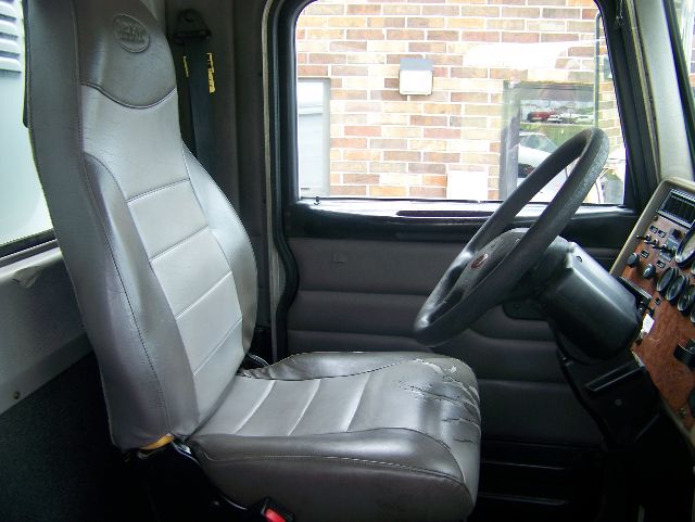 Peterbilt 335 truck interior with gray driver seat, steering wheel, and dashboard; visible door, window, and control panel.
