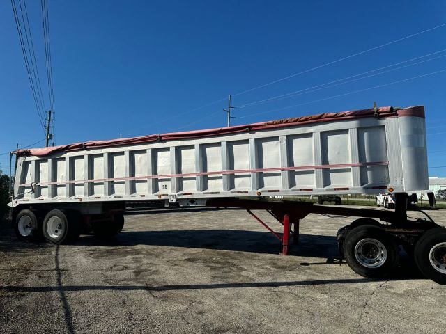 Dump trailer with metal sidewalls and a red tarp rolled along the top, mounted on a semi truck chassis.