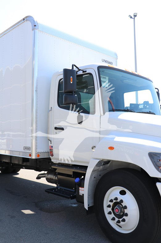 Truck cab and chassis side view showing white Hino L6 box truck with large side mirror, door handle, and front wheel visible.