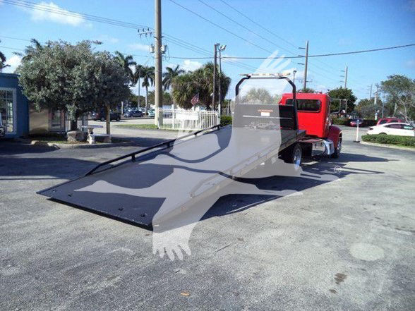 Red Peterbilt 337 tow truck with a large flatbed ramp extended, parked outdoors; background shows palm trees, utility poles, and a blue sky.