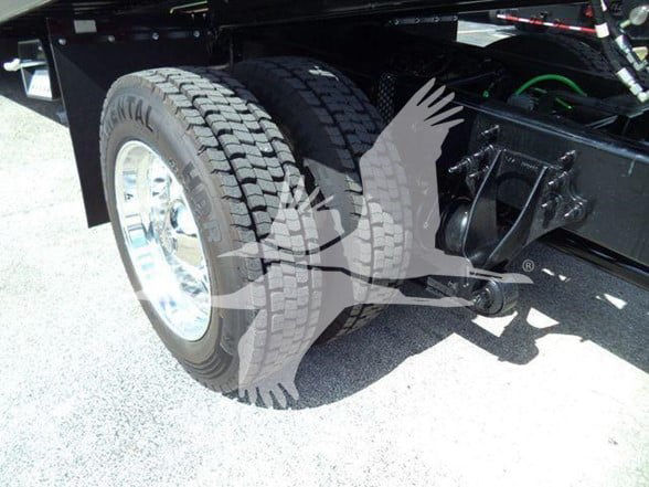 Partial rear axle area of a new International MV tow truck showing dual rear tires, chrome wheel rims, and suspension components.
