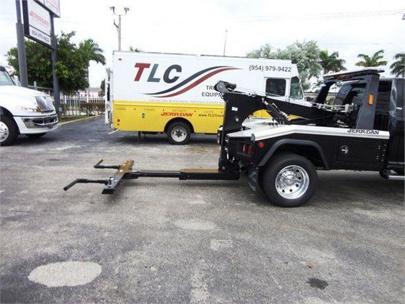 Ram 4500 tow truck with hook lift in foreground, TLC truck rental background signage on a sunny day.