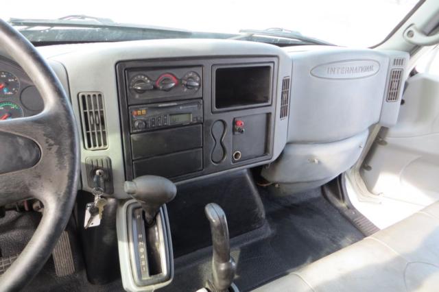 Truck interior dashboard with steering wheel on left, instrument cluster, central control panel, gear shifter, and empty display screen. On the glove box area is an embossed 'INTERNATIONAL' logo.