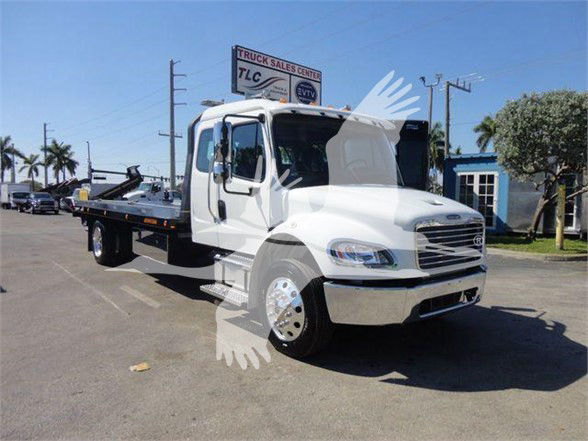 Tow truck chassis in lot with cab open and flatbed; visible text on sign in background reads 'TRUCK SALES CENTER'; no other legible labels on the vehicle.