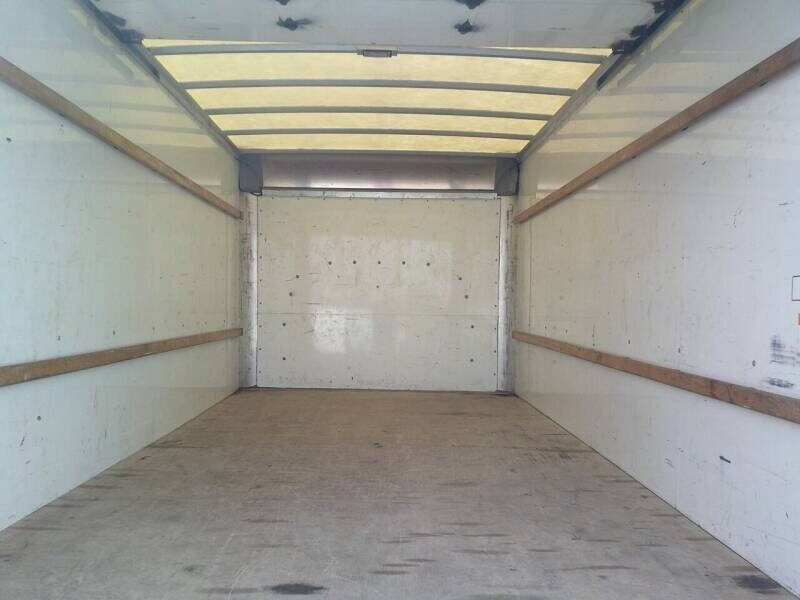 Box truck cargo area empty with white walls and wooden side rails, rear door closed.
