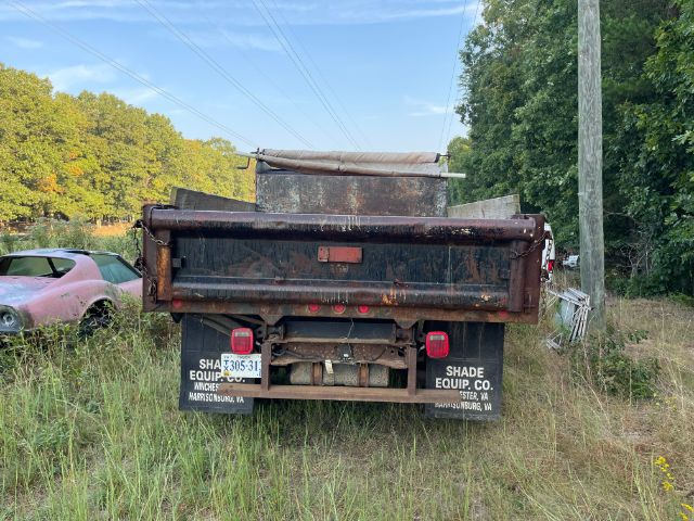 Dump truck bed showing rear view with tailgate and mud flaps, faded black paint, and rusted metal surface.