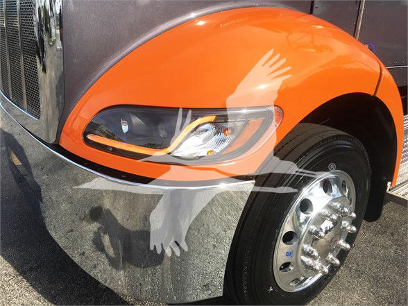 Front fender and headlight of a orange Peterbilt 337 truck with chrome bumper and wheel, showing partial view of headlight, fender, and wheel with hubcap.