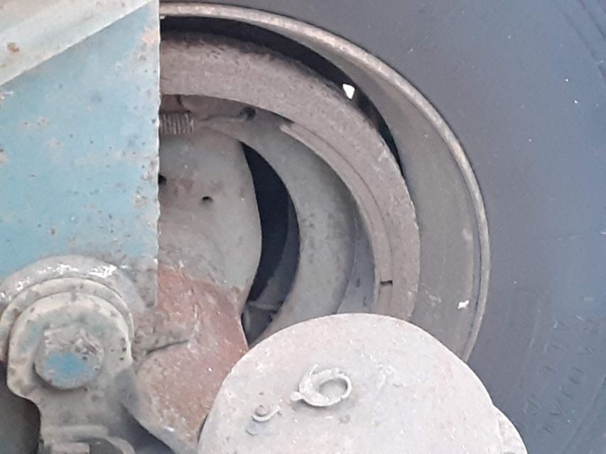 Wheel hub and drum area of a utility trailer showing a dusty, circular brake/drum assembly with a blue painted frame and a circular cap or cover.
