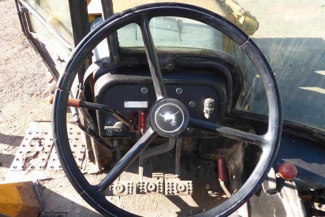Steering wheel and instrument cluster inside a John Deere 710B backhoe cab. Visible dashboard with pedals, levers, and hydraulic controls.