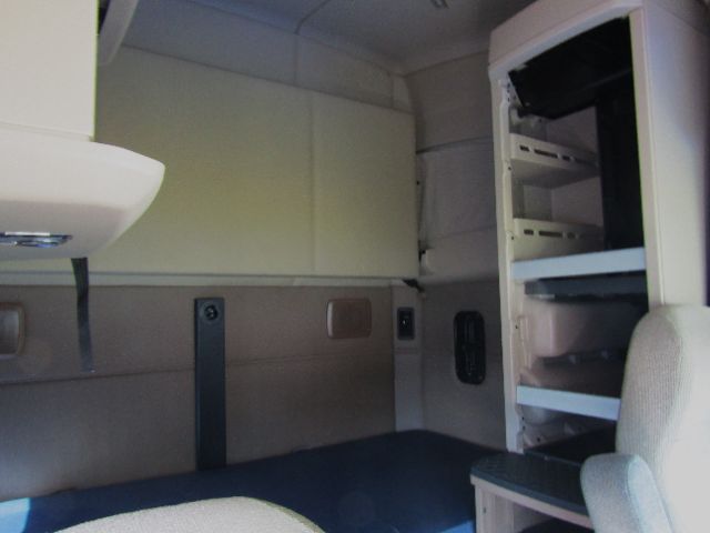 Kenworth truck cab interior showing sleeper area with storage shelves and seat.