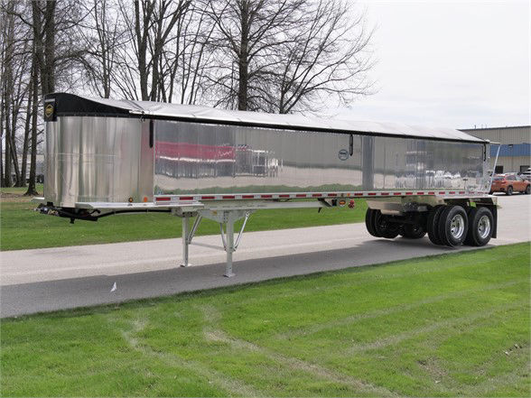 Trailer showing aluminum lightweight frameless dump trailer with polished sides and dual rear axles.