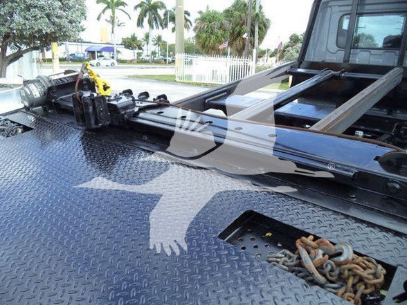 Tow truck bed with hydraulic winch and chain in foreground on a textured metal deck.