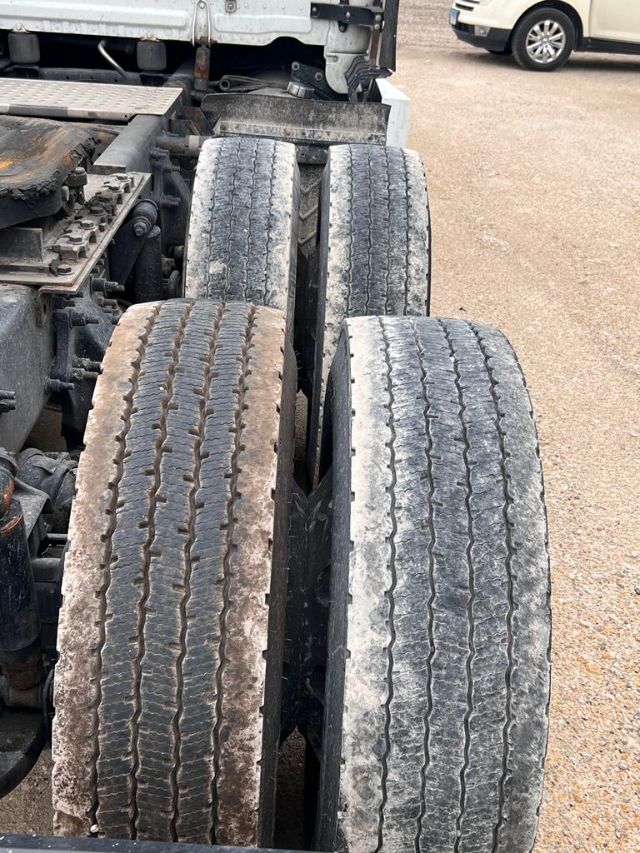 Freightliner Cascadia truck rear dual tires view; four tires visible on tandem axle with dirt and wear; some components of chassis and frame visible.