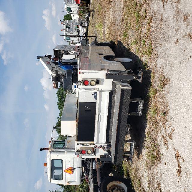 Back view of a white Ford utility tow truck with a crane, multiple compartments, and rear steps.