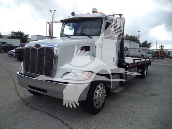 Peterbilt 337 tow truck front-left view with white cab and chrome grille, stake flatbed in background, VIN tag not visible.