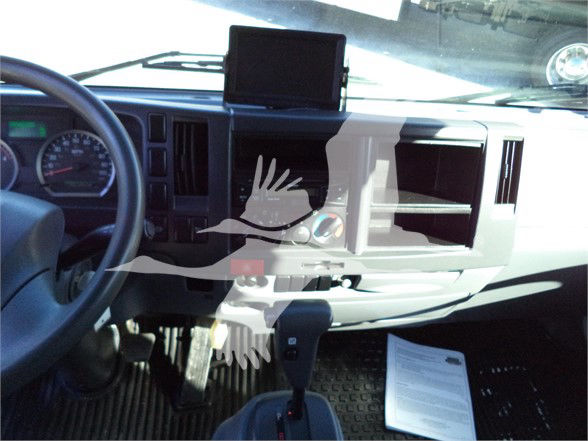 Isuzu NRR truck cabin interior showing dashboard with steering wheel, gear shifter, and a mounted screen. Dashboard vents and center area visible with some opened compartments; a paper document lies on the floor mat.